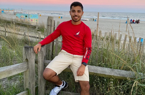 A young man sitting on a wooden fence at the beach.